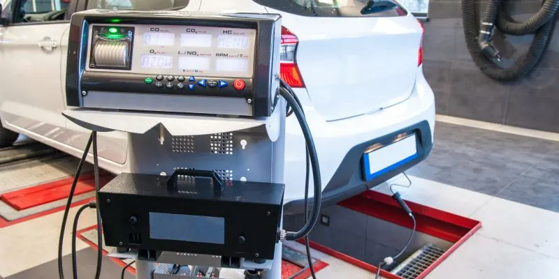 Messgerät zur Abgasuntersuchung steht hinter einem Auto auf dem Prüfstand in einer Werkstatt.