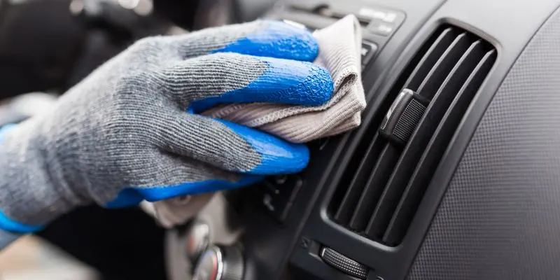 Person mit Arbeitshandschuhen reinigt das Armaturenbrett eines Autos mit einem Tuch.